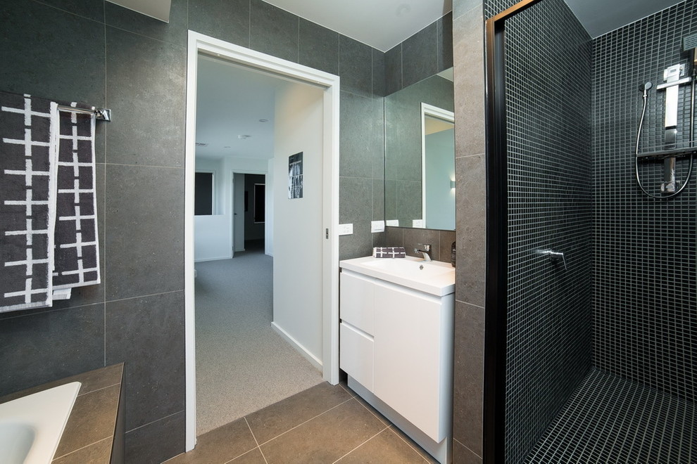 This is an example of a small contemporary kids bathroom in Canberra - Queanbeyan with flat-panel cabinets, white cabinets, a drop-in tub, an alcove shower, gray tile, porcelain tile, grey walls, porcelain floors, an integrated sink, solid surface benchtops, grey floor, a hinged shower door and white benchtops.