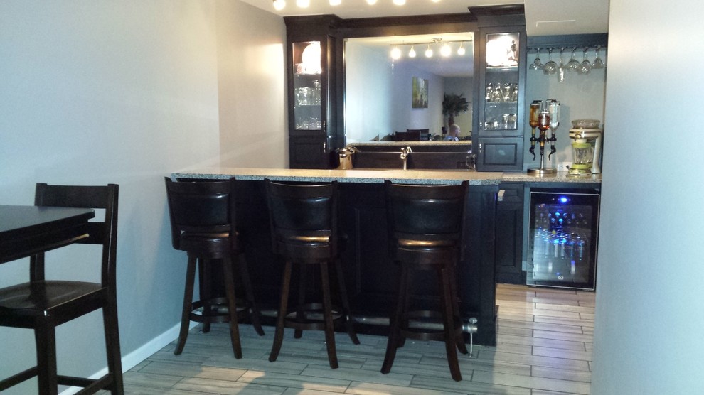 This is an example of a small contemporary single-wall seated home bar in St Louis with an undermount sink, raised-panel cabinets, black cabinets, granite benchtops and porcelain floors.