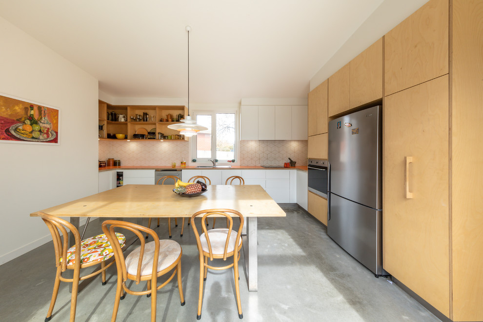 This is an example of a small contemporary l-shaped eat-in kitchen in Canberra - Queanbeyan with white cabinets, laminate benchtops, white splashback, ceramic splashback, stainless steel appliances, concrete floors, no island, grey floor, orange benchtop, a drop-in sink and flat-panel cabinets.