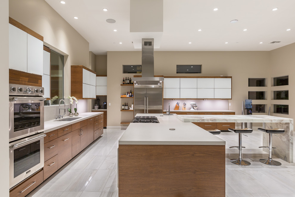 Large contemporary l-shaped open plan kitchen in Las Vegas with flat-panel cabinets, medium wood cabinets, solid surface benchtops, grey splashback, stainless steel appliances, ceramic floors and with island.