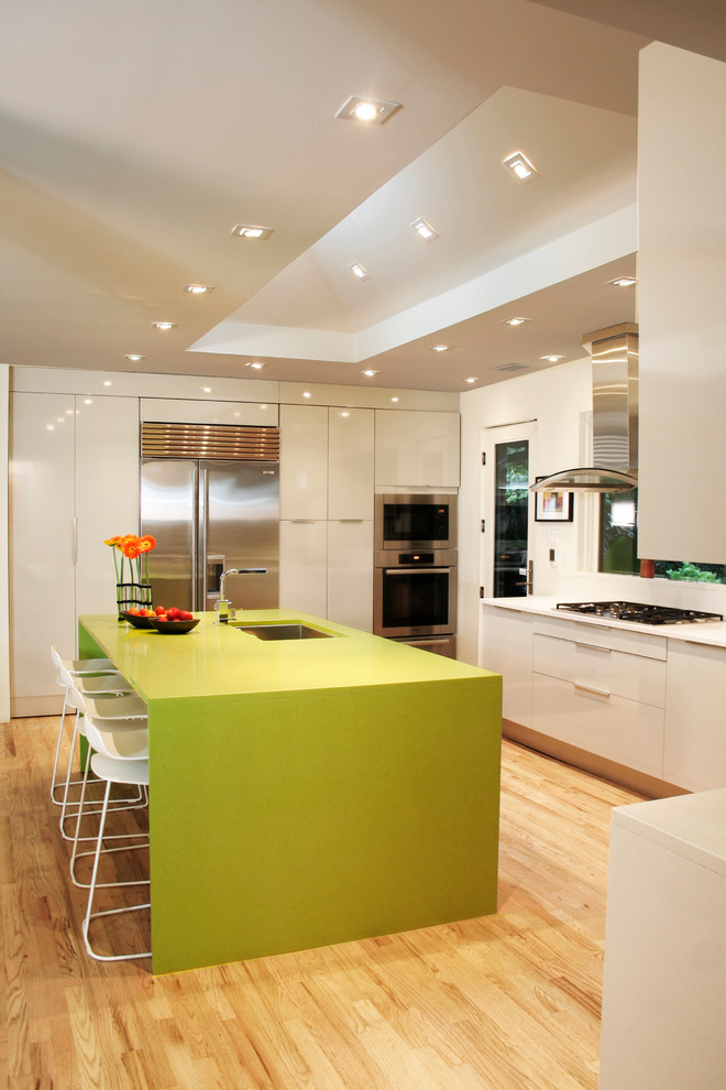 Photo of a contemporary u-shaped eat-in kitchen in DC Metro with an undermount sink, flat-panel cabinets, white cabinets, stainless steel appliances, light hardwood floors, with island, solid surface benchtops, white splashback and green benchtop.
