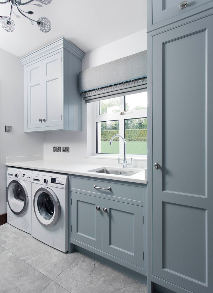 Design ideas for a mid-sized transitional l-shaped laundry room in Other with an integrated sink, shaker cabinets, blue cabinets, marble benchtops, grey splashback, marble splashback, porcelain floors and grey floor.