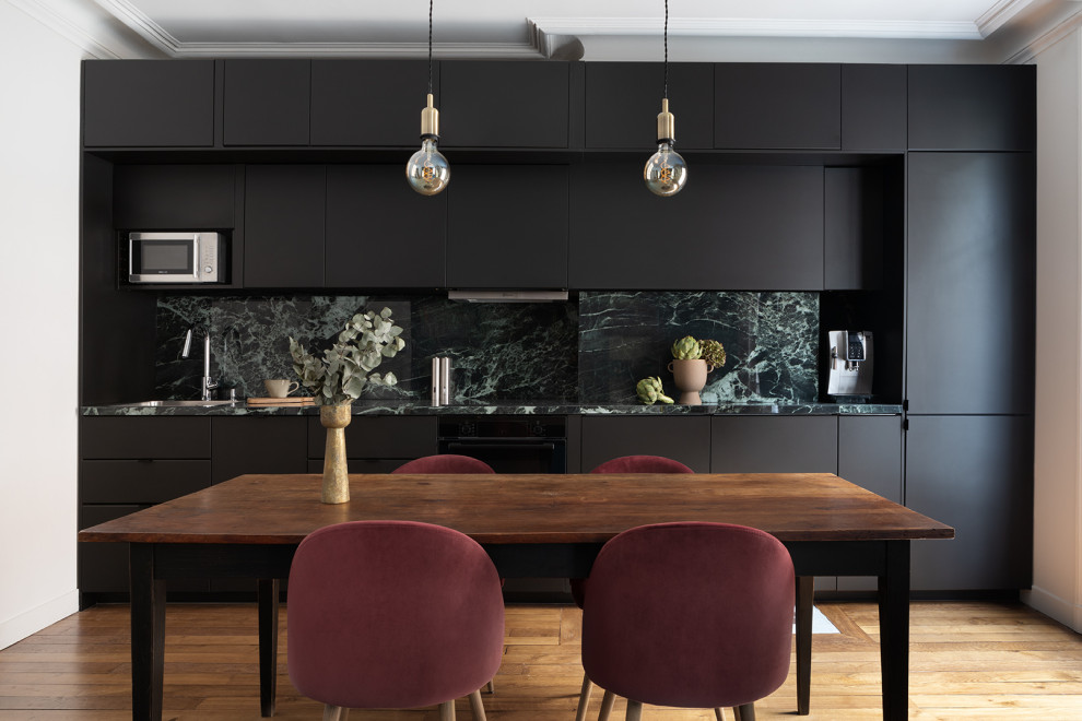 Eclectic single-wall open plan kitchen in Paris with an undermount sink, beaded inset cabinets, black cabinets, marble benchtops, green splashback, marble splashback, black appliances, light hardwood floors, no island and green benchtop.