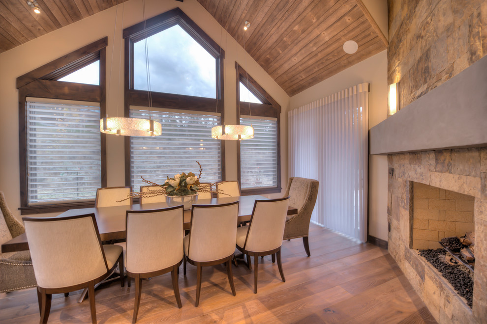 Photo of a mid-sized transitional open plan dining in Other with light hardwood floors, a two-sided fireplace and a stone fireplace surround.