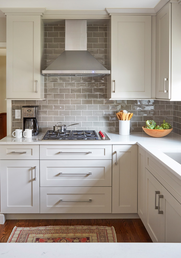 Photo of a mid-sized transitional u-shaped eat-in kitchen in Chicago with an undermount sink, shaker cabinets, white cabinets, quartz benchtops, grey splashback, subway tile splashback, panelled appliances, medium hardwood floors, a peninsula, brown floor and white benchtop.