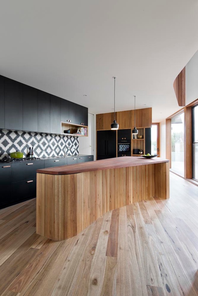 Inspiration for a mid-sized contemporary kitchen in Melbourne with flat-panel cabinets, black cabinets, wood benchtops, multi-coloured splashback, cement tile splashback, black appliances, medium hardwood floors and with island.