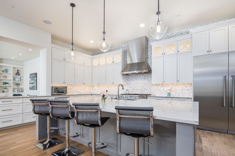 This is an example of a country l-shaped kitchen in Dallas with an undermount sink, shaker cabinets, white cabinets, grey splashback, stainless steel appliances, medium hardwood floors, with island, brown floor and grey benchtop.