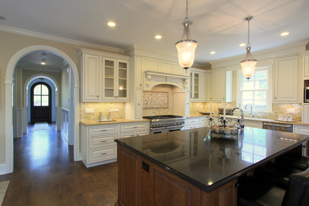 This is an example of a traditional kitchen in Chicago with raised-panel cabinets, white cabinets, beige splashback, a double-bowl sink, solid surface benchtops, subway tile splashback, stainless steel appliances and dark hardwood floors.