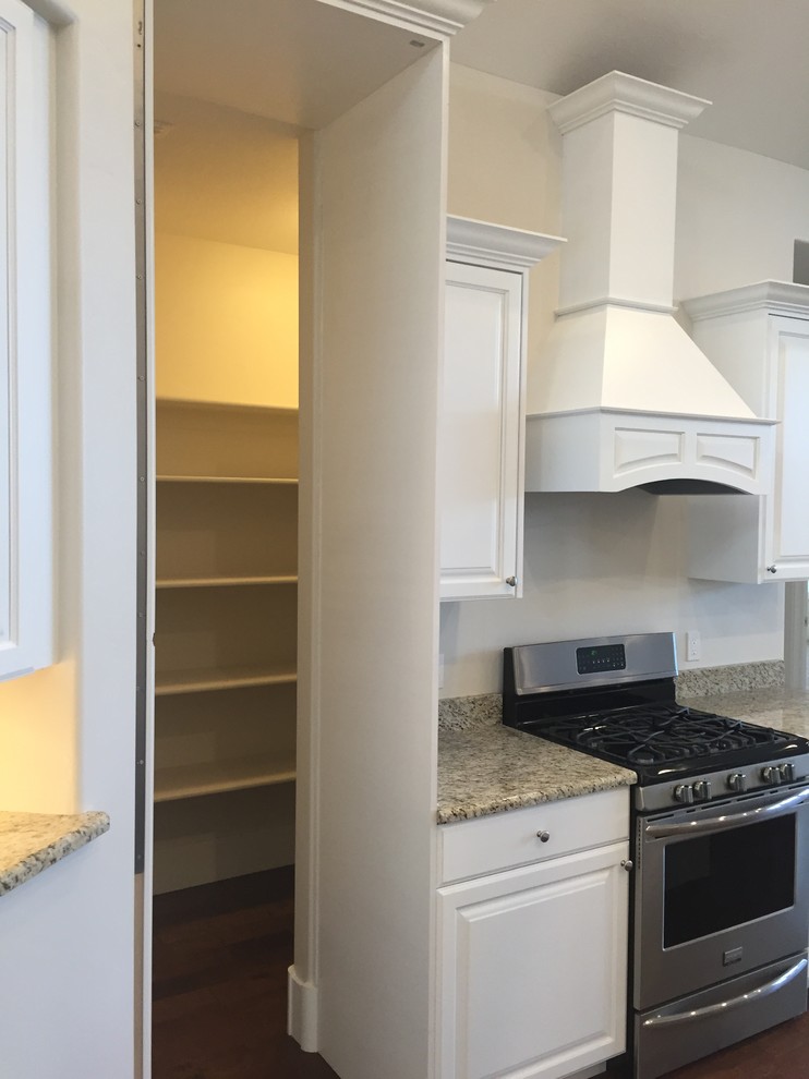 Foto på ett mellanstort amerikanskt kök, med en undermonterad diskho, luckor med upphöjd panel, vita skåp, granitbänkskiva, rostfria vitvaror, mörkt trägolv och en köksö