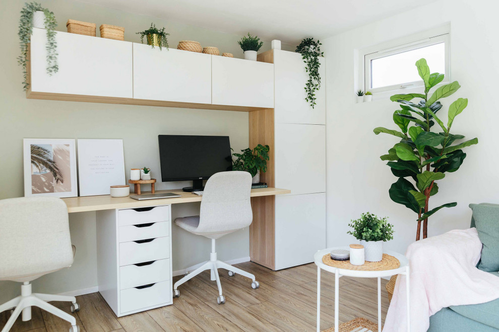 Diseño de despacho nórdico grande con paredes blancas, suelo de madera clara, escritorio empotrado y suelo beige