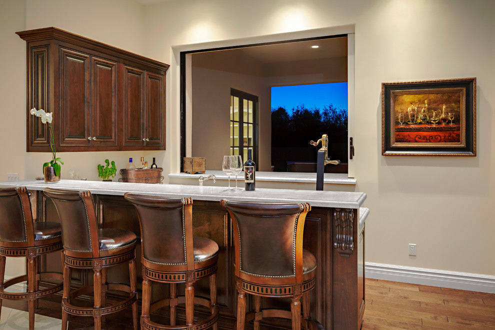 Photo of a mid-sized traditional l-shaped wet bar in Phoenix with beaded inset cabinets, medium wood cabinets, marble benchtops and medium hardwood floors.