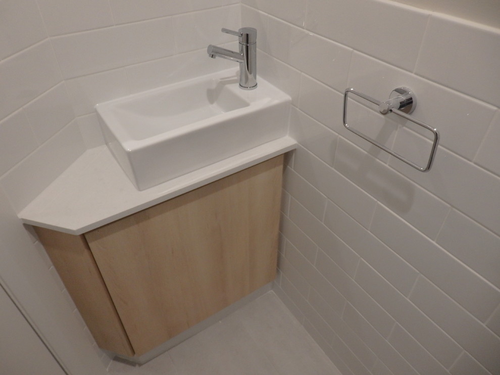 Immagine di un bagno di servizio nordico di medie dimensioni con ante lisce, ante in legno chiaro, piastrelle bianche, pareti bianche, lavabo a bacinella e top in quarzo composito