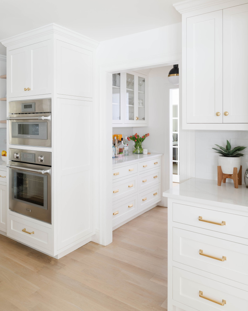 Idéer för att renovera ett stort vintage vit vitt kök, med en undermonterad diskho, luckor med infälld panel, vita skåp, bänkskiva i kvarts, vitt stänkskydd, stänkskydd i keramik, rostfria vitvaror, ljust trägolv och en köksö