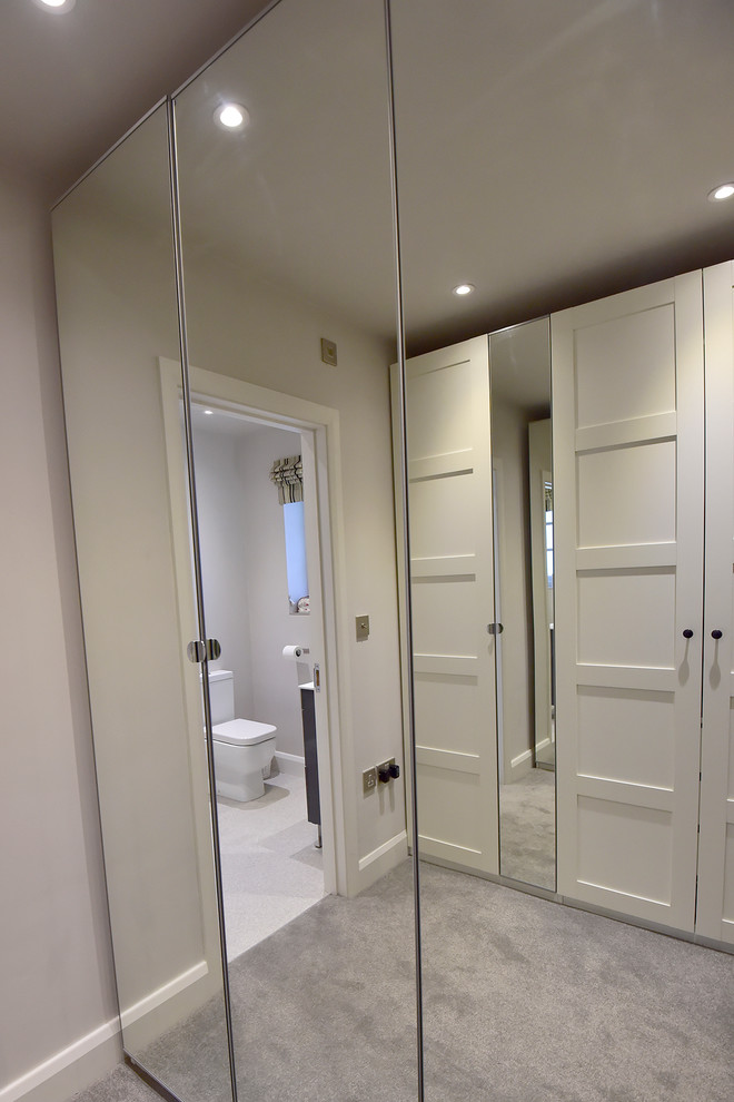 This is an example of a mid-sized contemporary gender-neutral dressing room in Hertfordshire with recessed-panel cabinets, white cabinets and carpet.