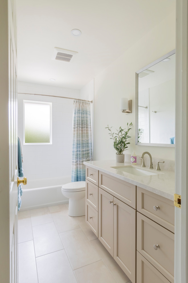Photo of a mid-sized transitional kids bathroom in New York with shaker cabinets, beige cabinets, a drop-in tub, a shower/bathtub combo, a two-piece toilet, white tile, subway tile, beige walls, porcelain floors, an undermount sink, engineered quartz benchtops, beige floor, a shower curtain, white benchtops, a niche, a single vanity and a built-in vanity.