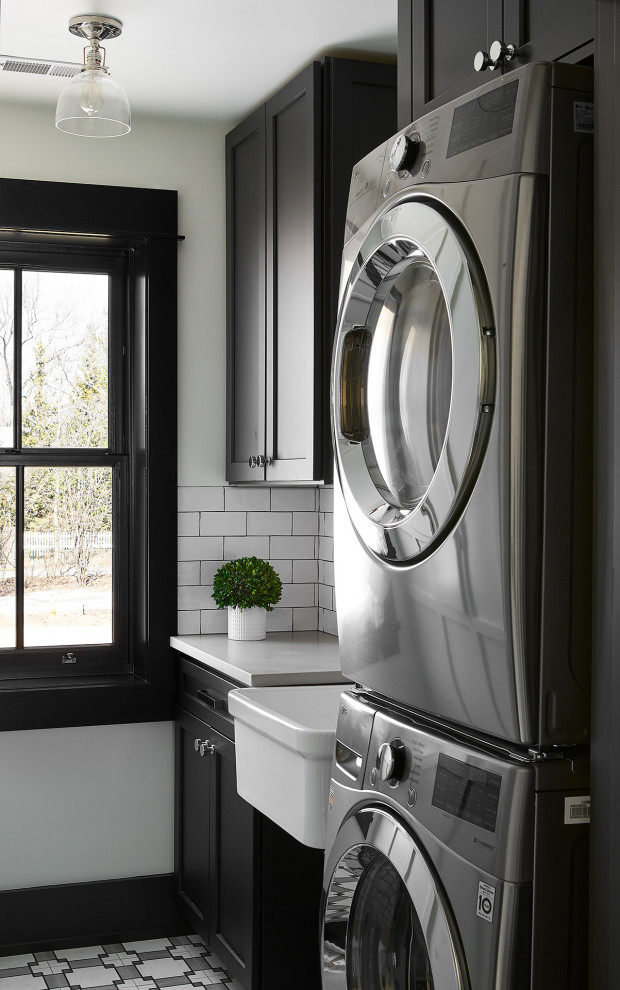 Modern inredning av en liten grå parallell grått tvättstuga enbart för tvätt, med en rustik diskho, skåp i shakerstil, svarta skåp, bänkskiva i kvarts, vitt stänkskydd, stänkskydd i keramik, vita väggar, betonggolv och en tvättpelare