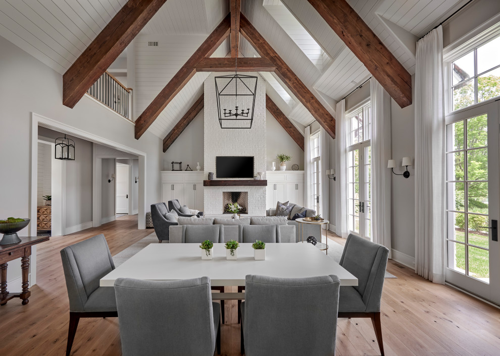 Diseño de sala de estar abierta y abovedada con paredes grises, suelo de madera clara y marco de chimenea de ladrillo
