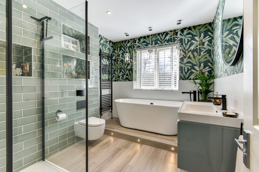 Example of a mid-sized kids' green tile and ceramic tile light wood floor, brown floor, single-sink and wallpaper bathroom design in Sussex with flat-panel cabinets, blue cabinets, a one-piece toilet, green walls, a drop-in sink, a hinged shower door, white countertops and a floating vanity