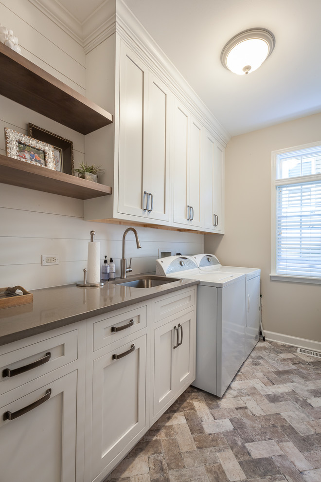 Design ideas for a mid-sized country utility room in Chicago with an undermount sink, white cabinets, quartz benchtops, beige walls, ceramic floors, a side-by-side washer and dryer, brown floor and shaker cabinets.