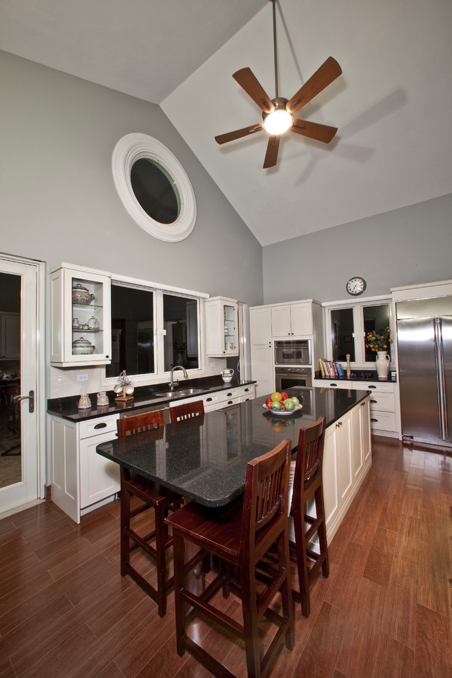 Example of a large transitional u-shaped ceramic tile enclosed kitchen design with an undermount sink, shaker cabinets, white cabinets, granite countertops, white backsplash, subway tile backsplash, stainless steel appliances and an island