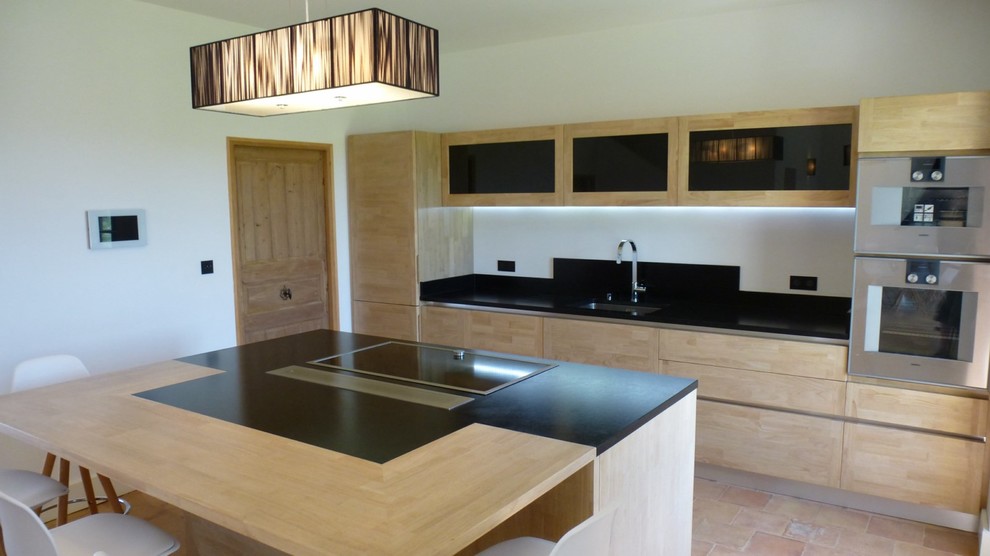 Photo of a large contemporary u-shaped open plan kitchen in Marseille with an integrated sink, flat-panel cabinets, light wood cabinets, granite benchtops, black splashback, stainless steel appliances, terra-cotta floors, with island, blue floor and black benchtop.