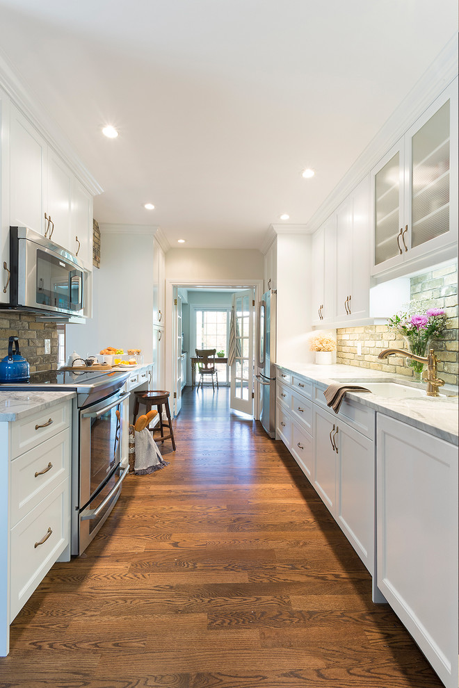 Photo of a mid-sized country galley separate kitchen in Other with shaker cabinets, white cabinets, quartzite benchtops, brown splashback, stainless steel appliances, medium hardwood floors, no island, brick splashback and a double-bowl sink.
