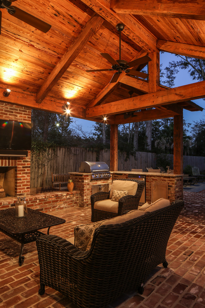 Large traditional backyard patio in New Orleans with an outdoor kitchen, brick pavers and a roof extension.