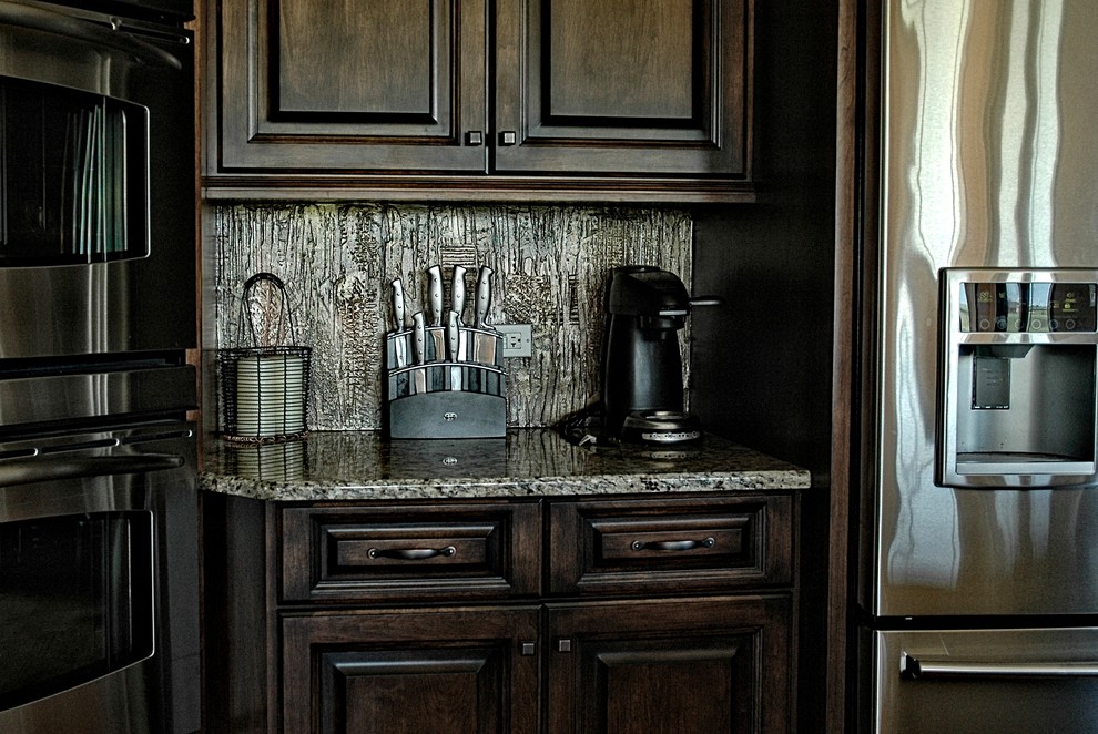 Kitchen - traditional kitchen idea in Phoenix with an undermount sink, raised-panel cabinets, dark wood cabinets, granite countertops, metallic backsplash, stainless steel appliances and an island