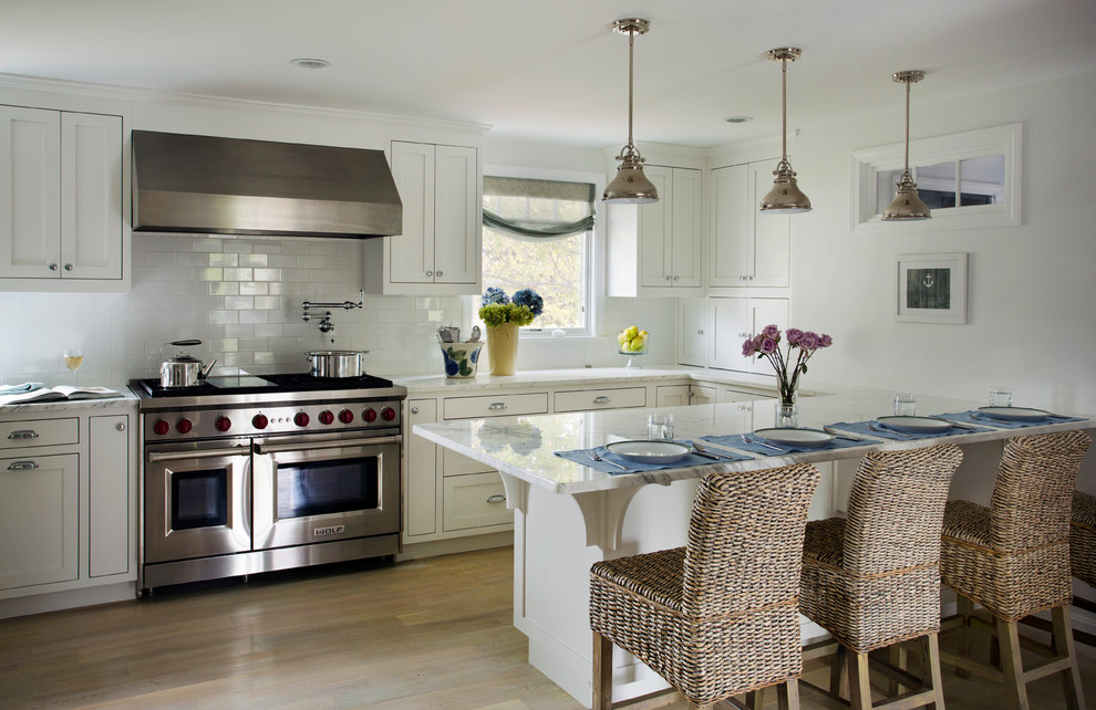 Inspiration for a mid-sized beach style u-shaped kitchen in Boston with recessed-panel cabinets, white cabinets, marble benchtops, white splashback, subway tile splashback, stainless steel appliances, light hardwood floors and a peninsula.