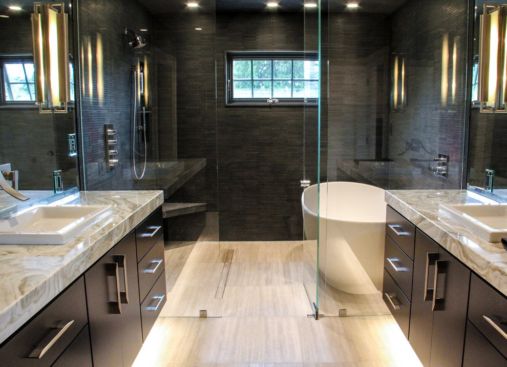 Inspiration for a large transitional master black tile and stone tile limestone floor freestanding bathtub remodel with flat-panel cabinets, dark wood cabinets, a two-piece toilet, gray walls, granite countertops, a vessel sink and a hinged shower door