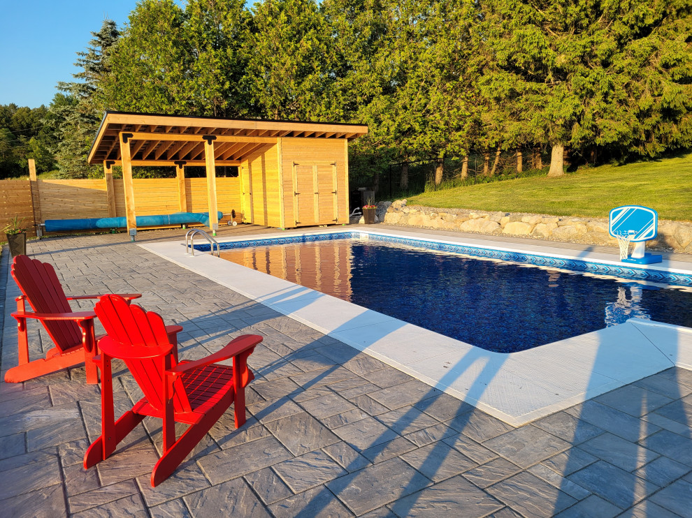 Example of a backyard concrete paver and rectangular pool house design