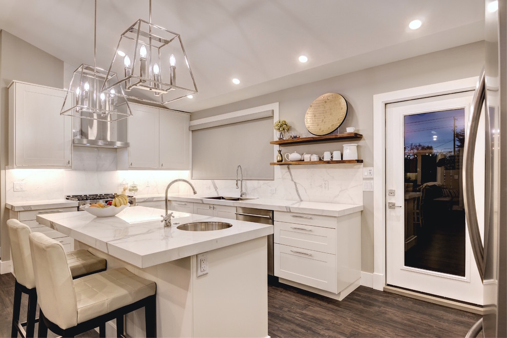 Example of a mid-sized transitional dark wood floor eat-in kitchen design in Calgary with a double-bowl sink, flat-panel cabinets, white cabinets, marble countertops, white backsplash, stainless steel appliances and an island