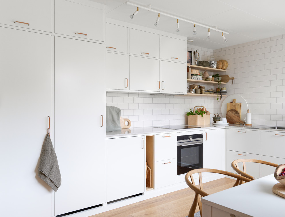 Photo of a mid-sized scandinavian l-shaped eat-in kitchen in Malmo with a single-bowl sink, flat-panel cabinets, white cabinets, quartz benchtops and stainless steel appliances.