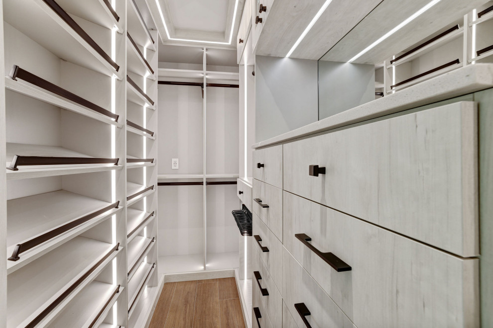 Diseño de armario vestidor unisex retro grande con armarios con paneles lisos, puertas de armario de madera clara, suelo de baldosas de cerámica y suelo marrón