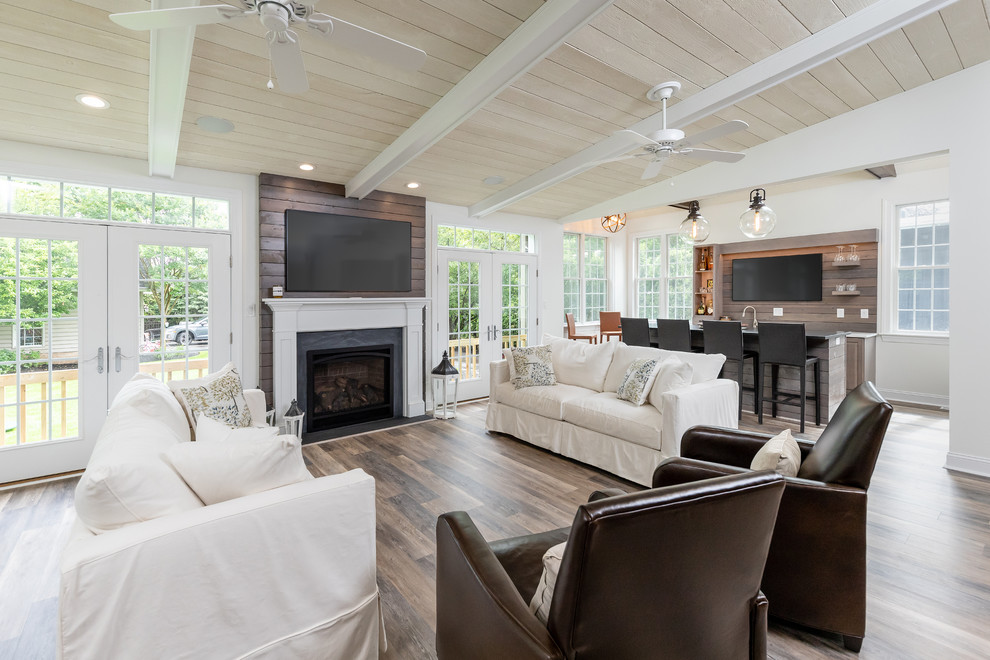 Large country open concept family room in Philadelphia with white walls, a standard fireplace, a wood fireplace surround, a wall-mounted tv, brown floor and medium hardwood floors.