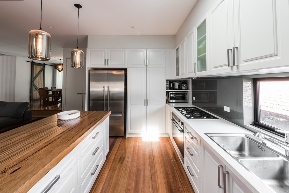 Inspiration for a mid-sized modern galley open plan kitchen in Melbourne with an undermount sink, raised-panel cabinets, white cabinets, quartz benchtops, grey splashback, white appliances, medium hardwood floors, with island and glass sheet splashback.