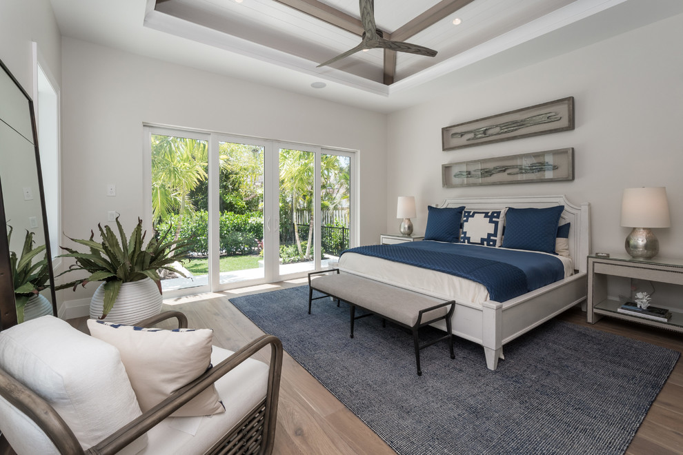 Photo of a beach style master bedroom in Miami with white walls, medium hardwood floors and brown floor.