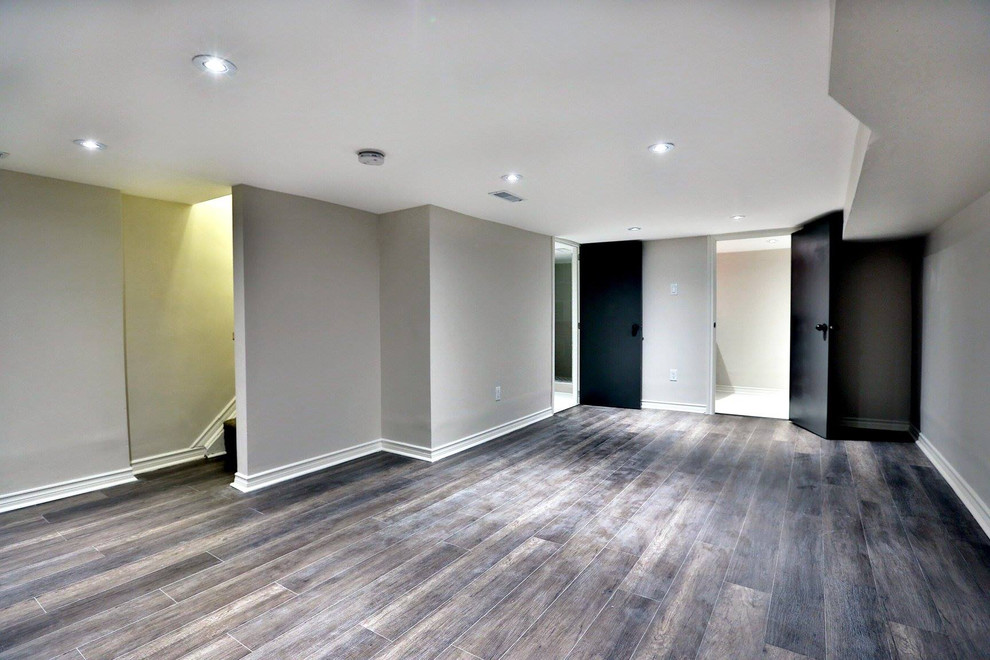 This is an example of a large transitional basement in Toronto with grey walls, medium hardwood floors, no fireplace and multi-coloured floor.