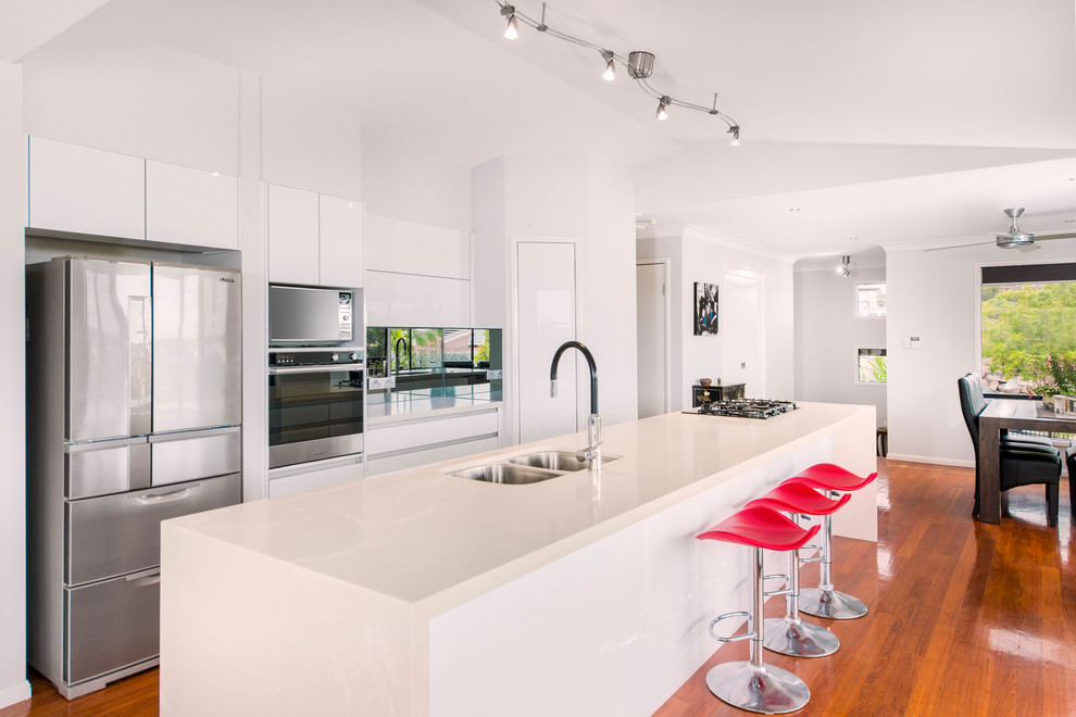 Design ideas for a large contemporary galley eat-in kitchen in Brisbane with an undermount sink, recessed-panel cabinets, white cabinets, quartz benchtops, mirror splashback, stainless steel appliances, light hardwood floors and with island.