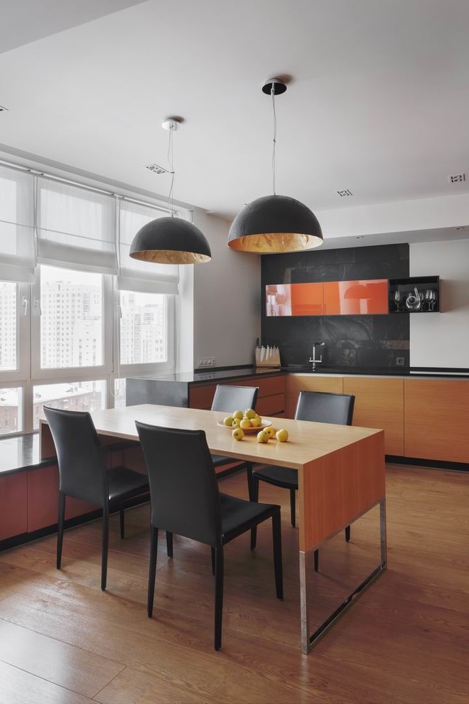 Design ideas for a mid-sized contemporary l-shaped eat-in kitchen in Moscow with flat-panel cabinets, solid surface benchtops, laminate floors, black benchtop, orange cabinets and black splashback.