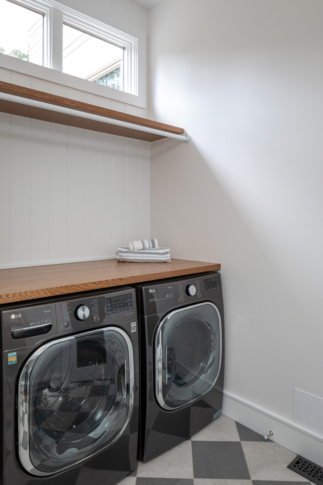 This is an example of a mid-sized transitional u-shaped dedicated laundry room in Raleigh with a farmhouse sink, shaker cabinets, white cabinets, wood benchtops, white splashback, shiplap splashback, white walls, porcelain floors, a side-by-side washer and dryer, brown benchtop and planked wall panelling.