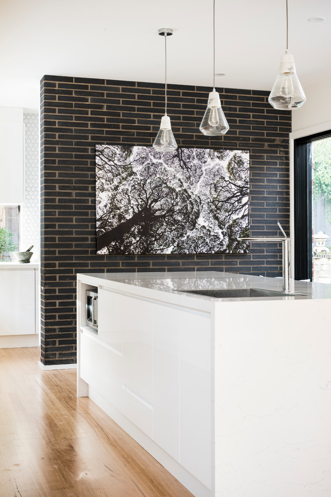 This is an example of a large contemporary l-shaped kitchen pantry in Melbourne with a drop-in sink, flat-panel cabinets, white cabinets, quartz benchtops, white splashback, cement tile splashback, black appliances, medium hardwood floors and with island.