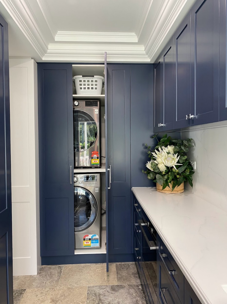 Idee per una piccola lavanderia multiuso con ante in stile shaker, ante blu, top in superficie solida, pavimento in travertino, lavatrice e asciugatrice a colonna, top bianco e soffitto a cassettoni