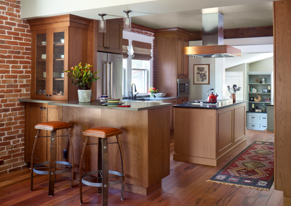 This is an example of an arts and crafts l-shaped kitchen in Denver with medium wood cabinets, stainless steel appliances, medium hardwood floors, with island and glass-front cabinets.