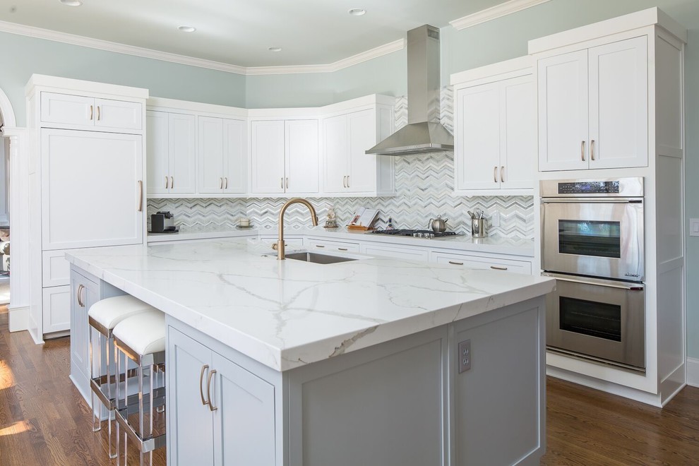 Example of a transitional l-shaped medium tone wood floor kitchen design with an undermount sink, shaker cabinets, white cabinets, multicolored backsplash, stainless steel appliances and an island