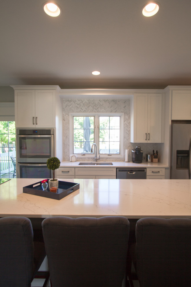 Open concept kitchen - transitional single-wall dark wood floor and brown floor open concept kitchen idea with an undermount sink, recessed-panel cabinets, white cabinets, quartzite countertops, gray backsplash, marble backsplash, stainless steel appliances and an island