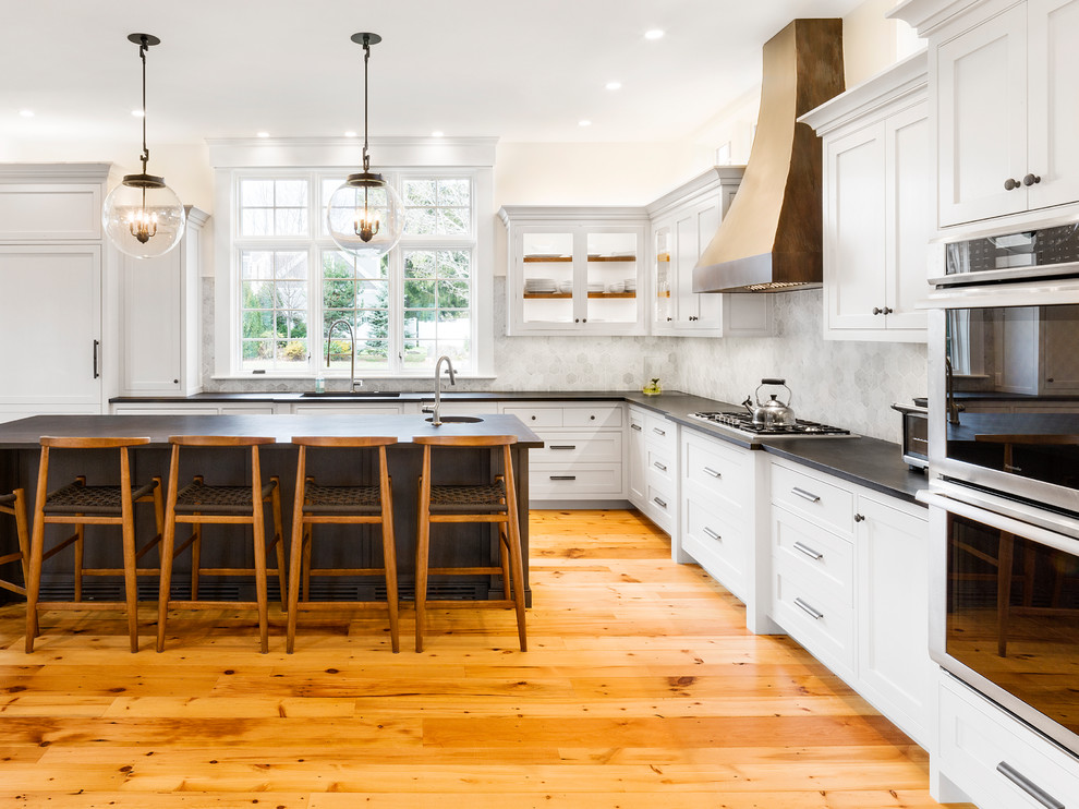 Example of a transitional l-shaped medium tone wood floor and orange floor kitchen design in Boston with an undermount sink, shaker cabinets, white cabinets, gray backsplash, stainless steel appliances and an island