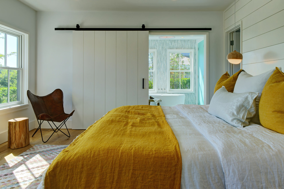 This is an example of a mid-sized beach style guest bedroom in Boston with white walls, medium hardwood floors and brown floor.