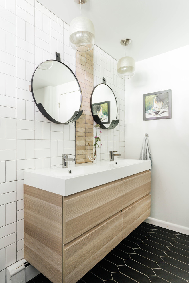 Photo of a midcentury bathroom in New York with flat-panel cabinets, light wood cabinets, white tile, white walls, a trough sink and black floor.