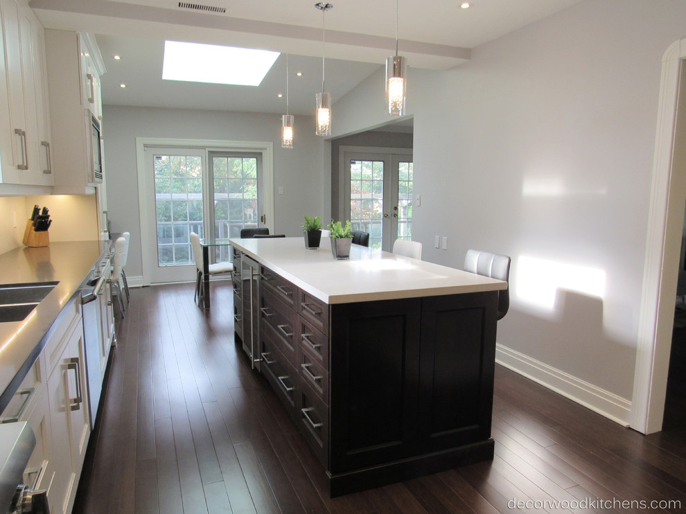 Example of a large transitional l-shaped dark wood floor enclosed kitchen design in Toronto with an undermount sink, shaker cabinets, white cabinets, quartz countertops, white backsplash, stone slab backsplash, stainless steel appliances and an island